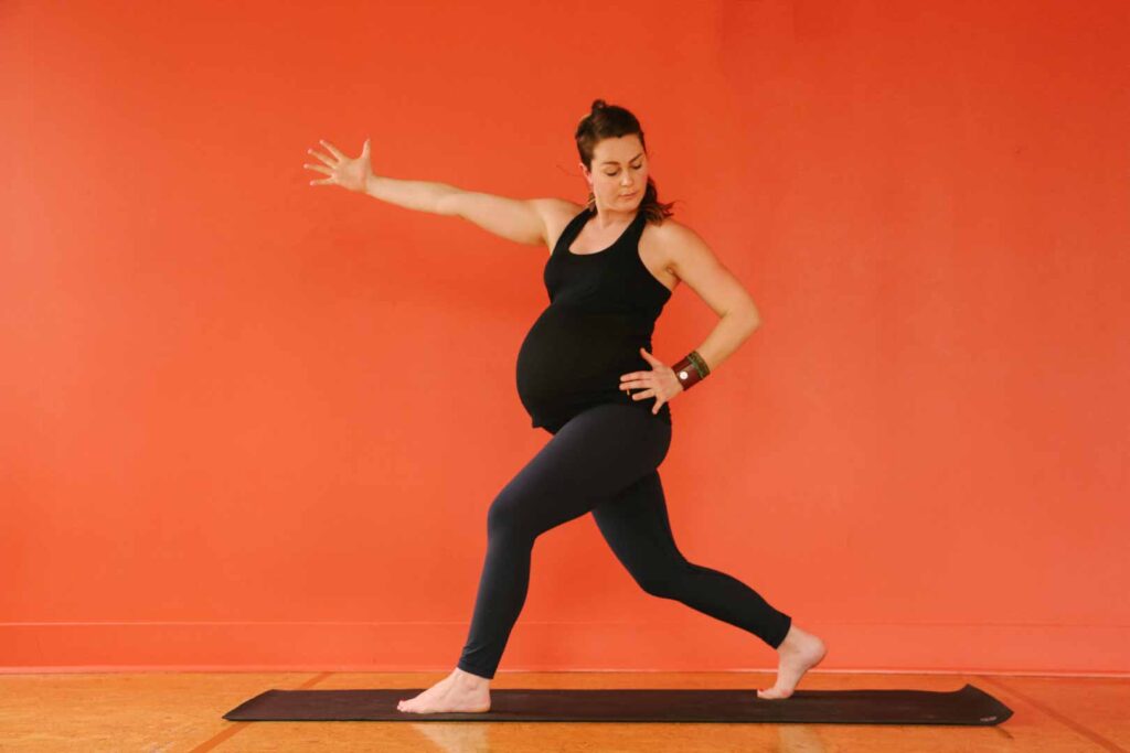 A pregnant woman doing yoga in crescent lunge.