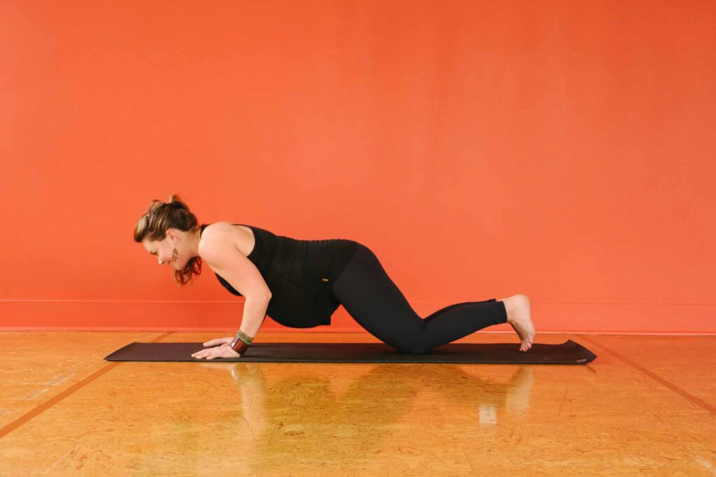 A pregnant woman doing chaturanga, or supported plank, in yoga studio.