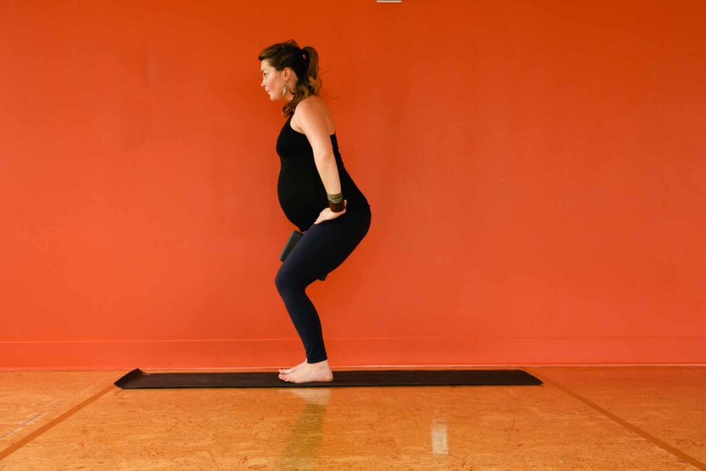 A pregnant woman doing chair pose in yoga studio.