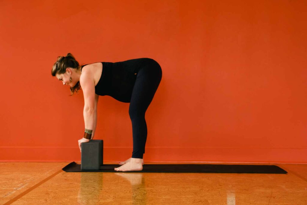 A pregnant woman doing supported forward fold pose, using blocks, in yoga studio.